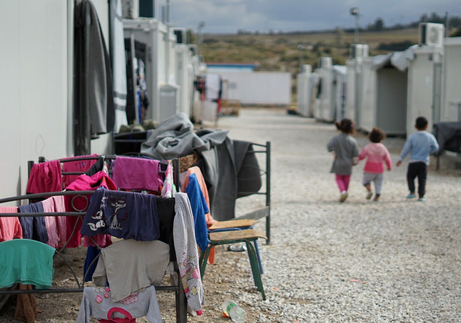 Three small children walking through a refugee camp.