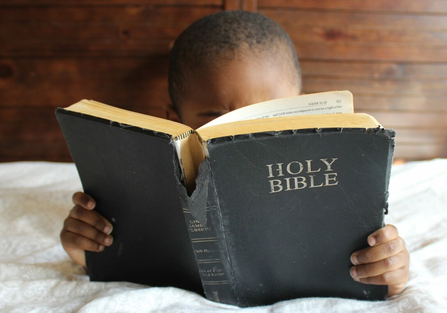 A black child sitting in bed reading a Bible